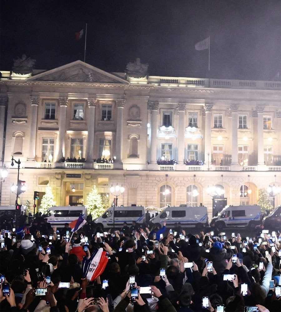 Các tuyển thủ Pháp đứng trên ban công tòa nhà vẫy chào đám đông người hâm mộ đứng cách đó vài mét. HLV Deschamps và đội trưởng thủ môn Hugo Lloris là những người đi ra chào fan trước, sau đó đến Mbappe và các đồng đội.