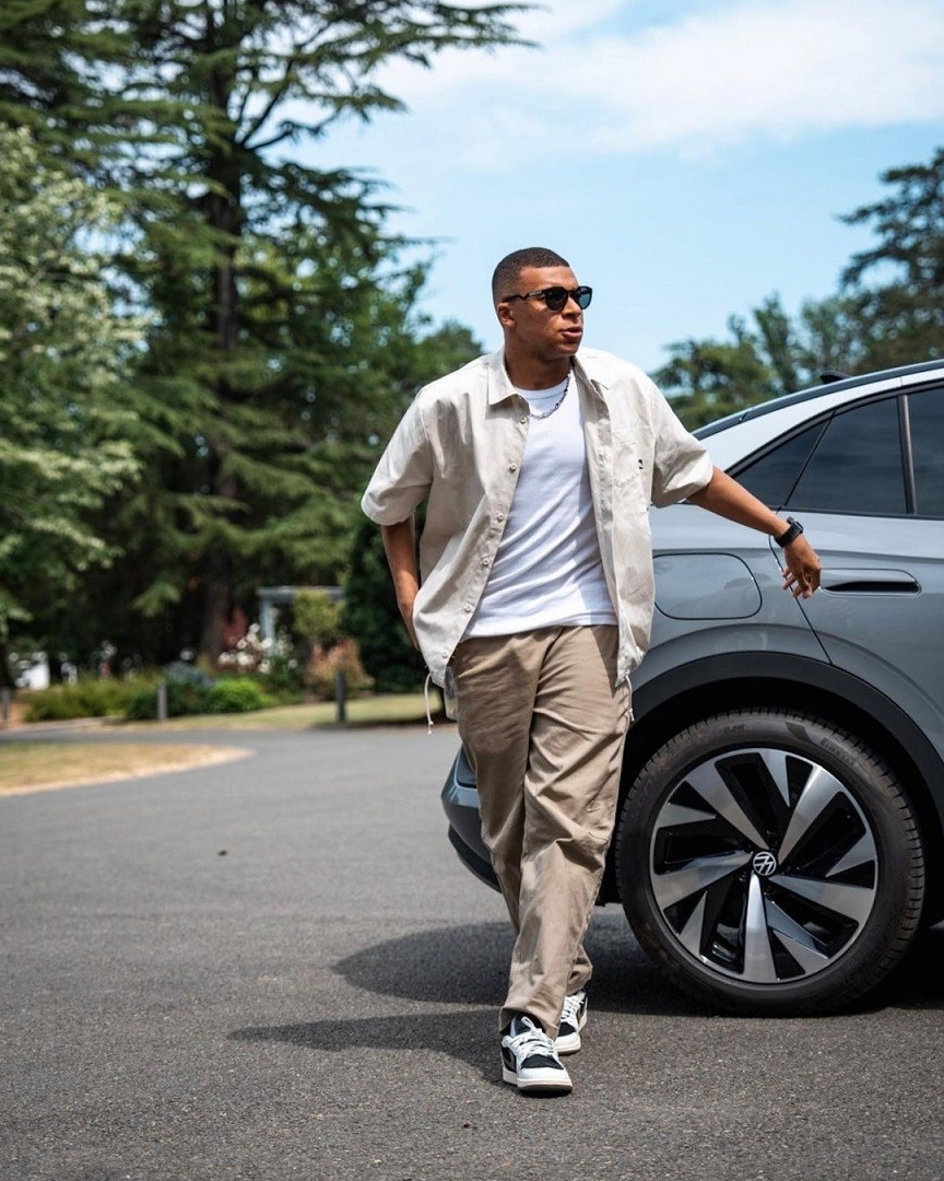 Trong loạt ảnh đăng trên trang cá nhân hôm 9/6, Kylian Mbappe đến đại bản doanh Clairefontaine, lò đào tạo trứ danh của bóng đá Pháp, nằm ở thị trấn nhỏ cách thủ đô Paris 50km về phía Tây Nam. Kylian Mbappe xuất hiện với set đồ trắng, beige gồm: áo thun, sơ mi tay ngắn, quần kaki, giày Nike Air Jordan 1, kính mát hiệu Oakley và vòng cổ Dior.