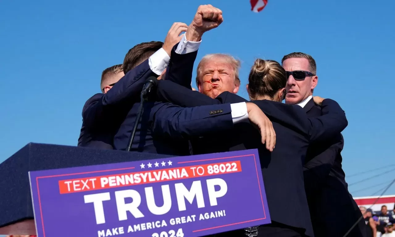 Ông Donal Trump giơ nắm đấm ra hiệu khi được các nhân viên mật vụ bao vây sau vụ nổ súng tại cuộc vận động tranh cử của ông ở Butler, Pennsylvania, ngày 13/7. Trong cuộc họp báo vào đêm muộn cùng ngày, Cục Điều tra Liên bang Mỹ (FBI) xác nhận vụ nổ súng khiến ứng cử viên tổng thống của đảng Cộng hòa Donald Trump bị thương trước đó là nỗ lực ám sát. Ông Trump an toàn, nghi phạm đã bị bắn hạ. Vụ việc khiến 1 khán giả thiệt mạng và 2 người khác bị thương. (Nguồn: AP) Ông Donal Trump giơ nắm đấm ra hiệu khi được các nhân viên mật vụ bao vây sau vụ nổ súng tại cuộc vận động tranh cử của ông ở Butler, Pennsylvania, ngày 13/7. Trong cuộc họp báo vào đêm muộn cùng ngày, Cục Điều tra Liên bang Mỹ (FBI) xác nhận vụ nổ súng k