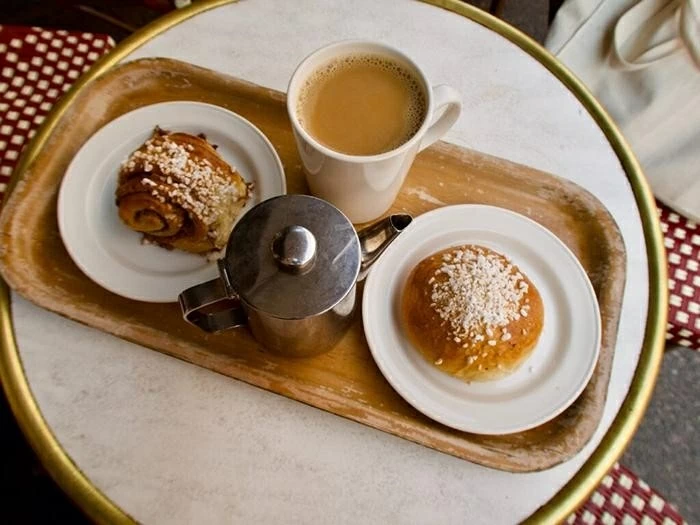Một khoảnh khắc Fika điển hình của Thụy Điển: cà phê nóng, bánh quế kanelbulle giản dị và khoảng dừng đủ chậm để con người kết nối với nhau, không áp lực, không phân biệt vai trò.