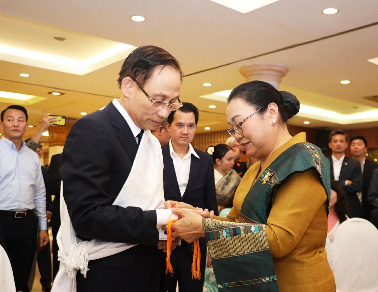 Đại sứ Khamphao Ernthavanh buộc chỉ cổ tay cho Bộ trưởng Ngoại giao Lê Hoài Trung cầu phúc và bình an. (Ảnh: Thành Long)