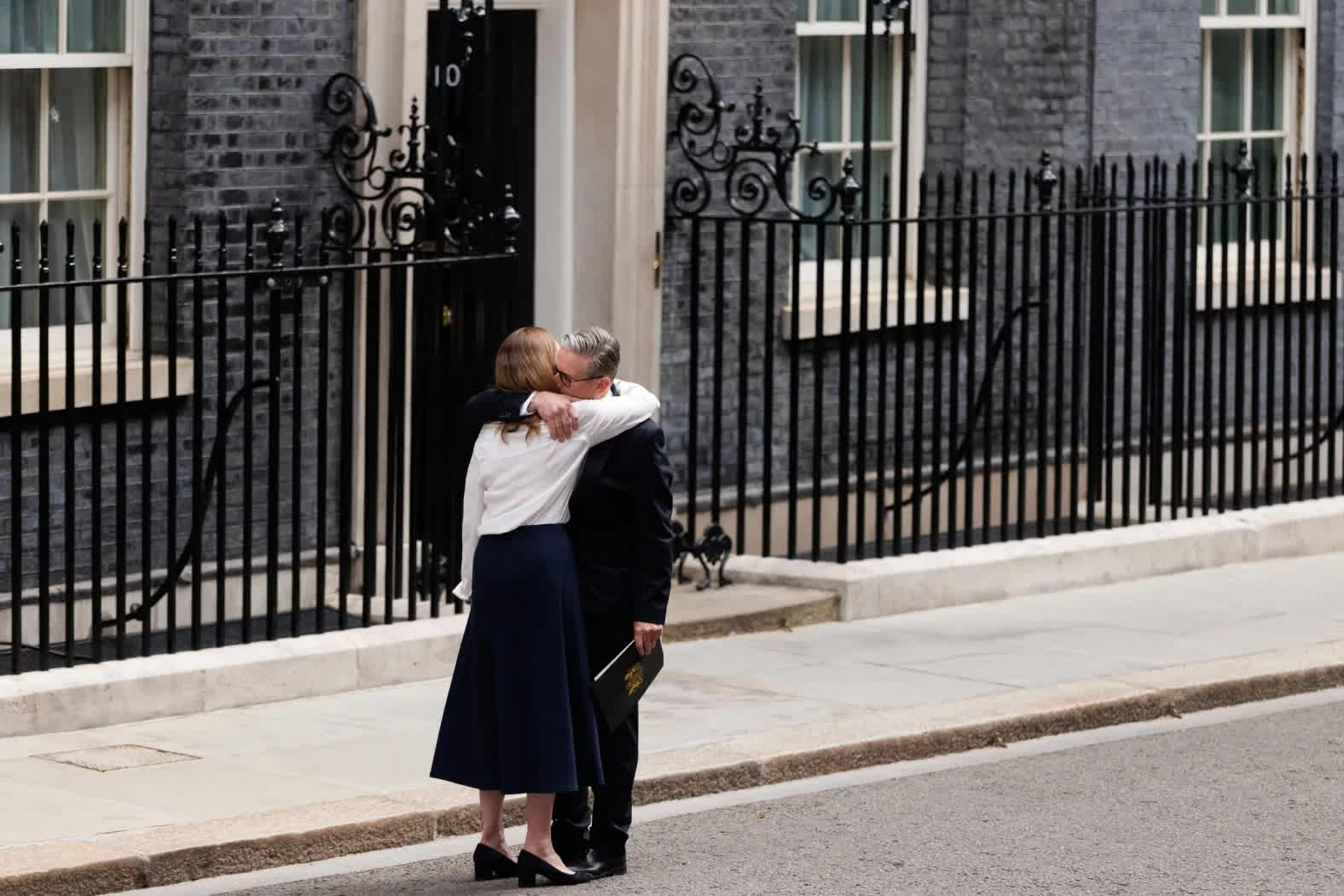 Keir Starmer ôm vợ, bà Victoria Starmer, bên ngoài số 10 phố Downing ở London sau khi tuyên bố từ chức vào thứ Hai, 22/6. Quyết định từ chức của ông Starmer được đưa ra sau kết quả bầu cử địa phương trong tháng 5 đầy thất vọng đối với đảng của ông. Với diễn biến này, United Kingdom đang trên đà có nhà lãnh đạo thứ sáu chỉ trong vòng bảy năm. (Nguồn: Getty Imgaes)