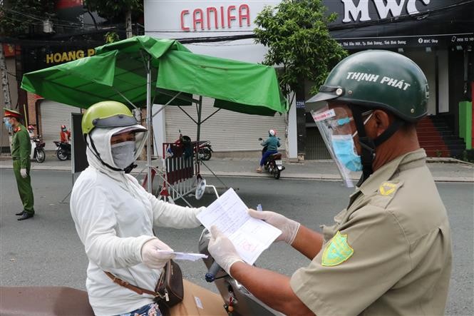 Một người phụ nữ đi chợ trình giấy có giấy tiêm đủ vaccine cho lực lượng kiểm tra trên đường Yersin, thành phố Thủ Dầu Một, tỉnh Bình Dương. (Nguồn: TTXVN)