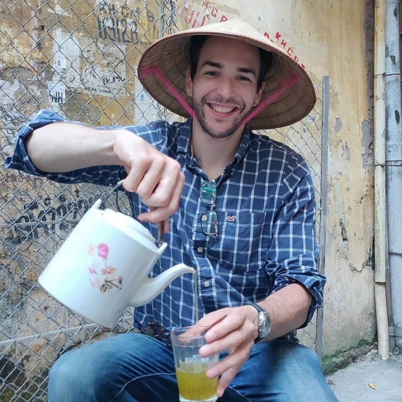 Will Courageux vừa thường thức trà đá vừa đội nón lá Việt Nam trong một bộ ảnh được chụp tại Hà Nội. (Ảnh: Will Courageux)