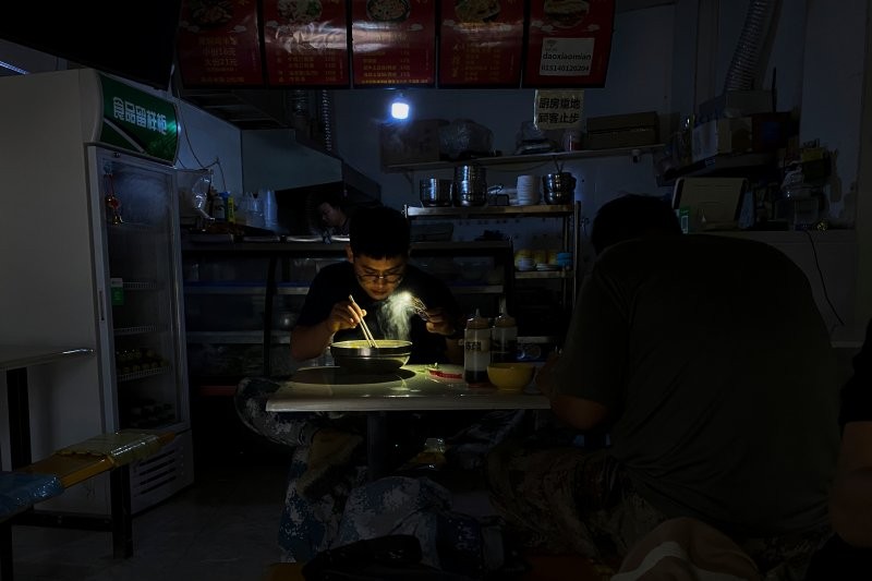 (11.26) Một người đàn ông Trung Quốc ăn nốt bát mỳ của mình dưới ánh đèn leo lét từ điện thoại sau khi căn phòng mất điện. (Nguồn: AP)