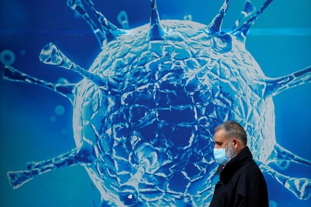 Người dân đeo khẩu trang đi ngang qua hình ảnh minh họa cho virus SARS-CoV-2. (Ảnh: Reuters)