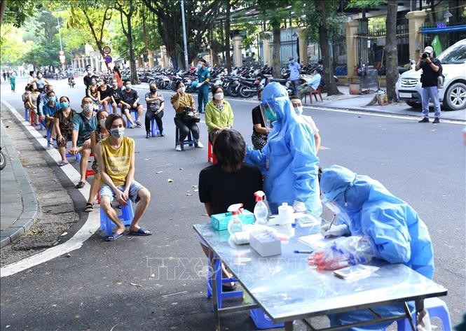 Nhân viên y tế lấy mẫu xét nghiệm sàng lọc Covid-19 cho người dân các hộ khu vực trước cổng Bệnh viện Việt Đức. (Nguồn: TTXVN)