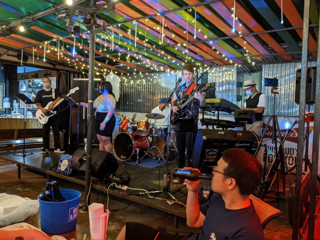 Học giả Hàn Quốc Shin Hee-seok thưởng thức bia trong khi xem ban nhạc địa phương, Yuppies và Deloreans, biểu diễn tại Lobster & Grill ở trung tâm thành phố Tumon. (Lyric Li / The Washington Post).