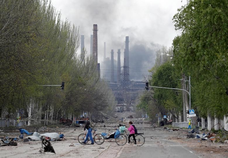 Người dân dắt xe đạp trên đường phố khi khói bốc lên từ nhà máy thép Azovstal ở thành phố cảng phía Nam Mariupol, Ukraine, ngày 2/5. (Nguồn: Reuters)